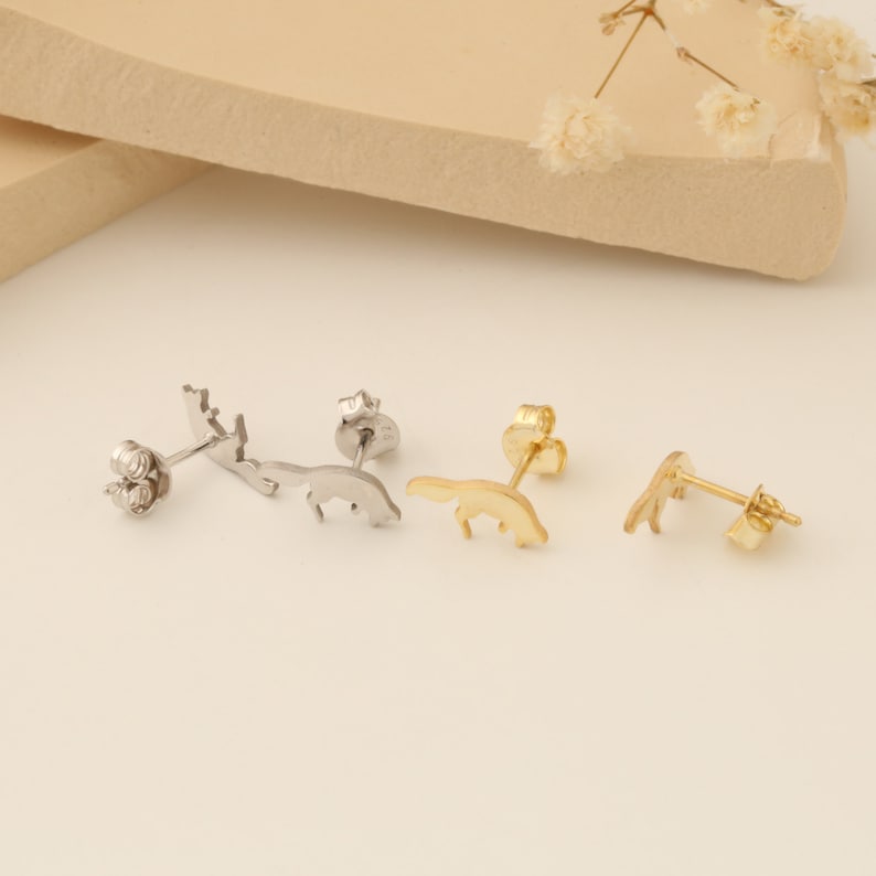 May include: Three pairs of small animal stud earrings. One pair is silver with a deer design, one pair is gold with a fox design, and one pair is gold with a bear design.