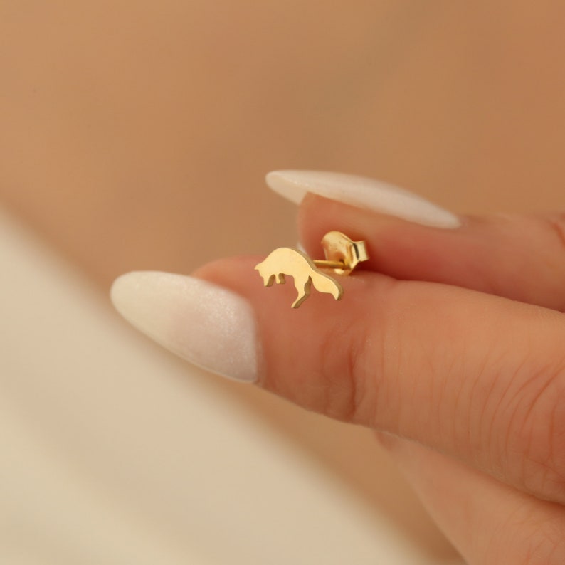 May include: A gold-toned fox silhouette earring. The earring is a simple, minimalist design.