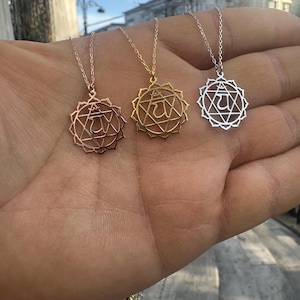 Peut inclure: Trois colliers avec des pendentifs chakra en or rose, or et argent. Chaque pendentif présente un design géométrique avec un symbole central, suspendu à de fines chaînes. Les colliers sont présentés sur un fond neutre.