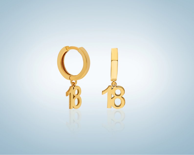 May include: A pair of gold hoop earrings with a dangling charm of the number 18.