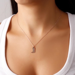 May include: A silver necklace with a boot pendant. The necklace is on a model wearing a white tank top.