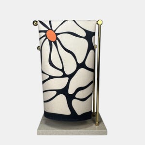 Op de afbeelding: Een decoratieve handdoek met een groot bloemmotief in zwart en oranje op een crèmekleurige achtergrond. De handdoek wordt getoond op een goudkleurige metalen standaard met een marmeren voet.