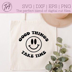 May include: A white tote bag with black text that reads "GOOD THINGS TAKE TIME" with a black smiley face in the center.