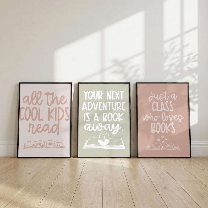May include: Three rectangular wall art prints in black frames. The left print is light pink with the text "all the COOL KIDS read" and a book icon. The center print is sage green with "YOUR NEXT ADVENTURE IS A BOOK away." and a book icon. The right print is dusty rose with "Just a CLASS who loves BOOKS" and a book icon.