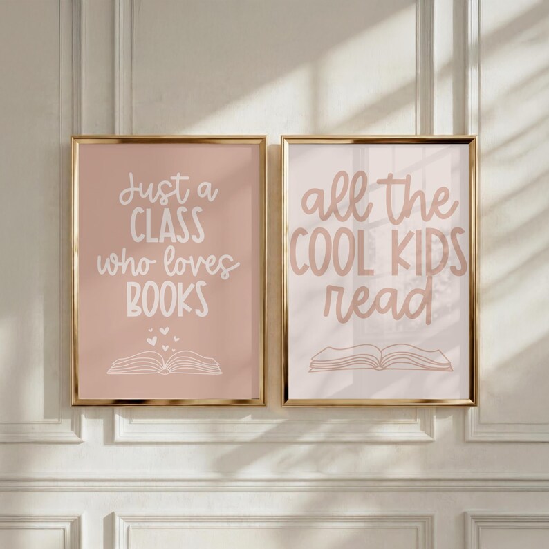 May include: Two framed wall art prints with gold borders. The left print has a dusty rose background with white text reading Just a CLASS who loves BOOKS and a line drawing of an open book. The right print has a light pink background with dark pink text reading all the COOL KIDS read and a line drawing of an open book.