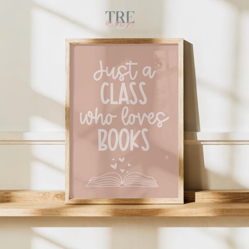 May include: A rectangular wall art print in a light wooden frame featuring a dusty rose background with white text that reads Just a CLASS who loves BOOKS, accompanied by a simple line drawing of an open book and several small floating hearts.