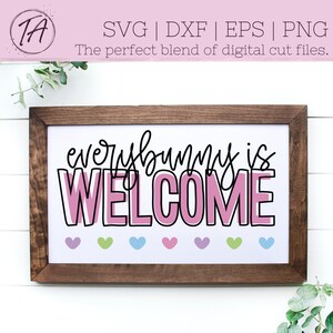 Może przedstawiać: Drewniany znak w ramie z tekstem "everybunny is WELCOME" w r&oacute;żowych i czarnych literach. Na dole znaku znajduje się sześć małych r&oacute;żowych, zielonych i niebieskich serc.