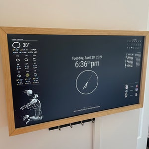 Puede incluir: Un reloj digital negro con una esfera y agujas blancas, que muestra la hora 6:36 pm. El reloj está montado en una pared con un marco de madera. La fecha es martes, 20 de abril de 2021. El reloj también muestra un pronóstico del tiempo con una temperatura de 38 grados Fahrenheit y un cielo nublado.