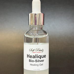 May include: A clear glass bottle with a white label featuring the text "Healique Bio-Silver Healing Gel" and "Soft Petalz Organic Cosmetics." The bottle has a silver dropper and a white top. The product is 30 ml.