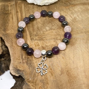May include: A bracelet made with amethyst, rose quartz, and hematite beads. The bracelet has a silver four-leaf clover charm.