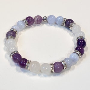May include: A beaded bracelet featuring a mix of purple, white, and light blue gemstones. The bracelet includes silver-toned spacers with clear crystal accents. The gemstones are arranged in a circular pattern, creating a stylish accessory.
