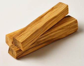 Puede incluir: Tres piezas rectangulares de madera marrón claro, posiblemente Palo Santo, apiladas sobre una superficie blanca. La madera tiene un patrón de vetas natural y una textura ligeramente rugosa. Los extremos de las piezas de madera están cortados en ángulo.