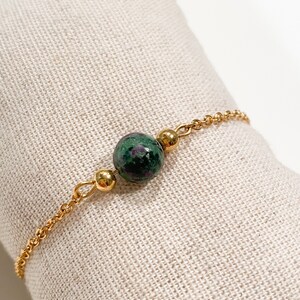 May include: A gold chain bracelet with a single green and pink gemstone bead.