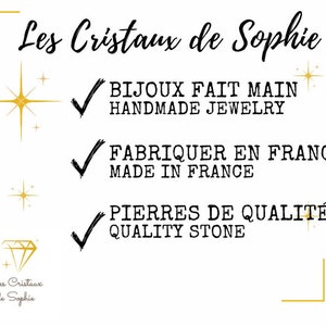 May include: A white background with gold stars and a gold diamond shape. The text "Les Cristaux de Sophie" is in black cursive font. Below the text are three checkmarks with text in black font: "BIJOUX FAIT MAIN HANDMADE JEWELRY", "FABRIQUER EN FRANCE MADE IN FRANCE", and "PIERRES DE QUALIT&Eacute; QUALITY STONE".