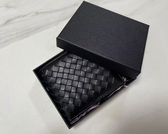 Peut inclure: Un portefeuille en cuir noir avec un motif tissé est présenté dans une boîte noire.