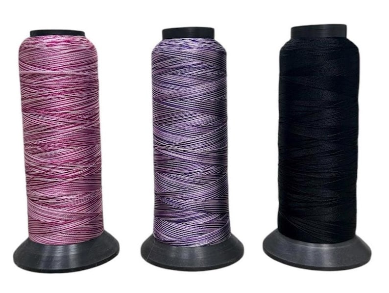 May include: Three spools of thread, one pink and white, one purple and white, and one black. The spools are all on a white background.
