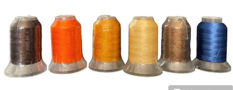 May include: Seven spools of thread in different colors. The spools are arranged in a row from left to right: dark brown, orange, gold, beige, brown, and blue.