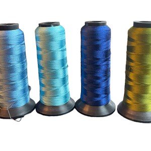 May include: Four spools of thread in different shades of blue and green. The spools are all the same size and have black plastic bases.