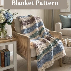 May include: A striped chunky knit blanket in blue, cream, and brown is draped over a wooden armchair. The blanket features the text "Driftwood Dusk Blanket Pattern". The chair is in a living room setting.