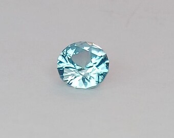 Può includere: Una pietra preziosa blu chiaro con taglio rotondo e molte sfaccettature.