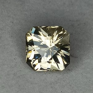 May include: A light green gemstone with a square shape and a faceted cut. The gemstone has a star-like pattern in the centre.