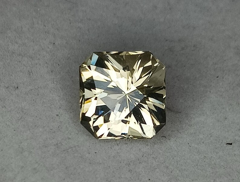 May include: A light green gemstone with a square shape and a faceted cut. The gemstone has a star-like pattern in the centre.