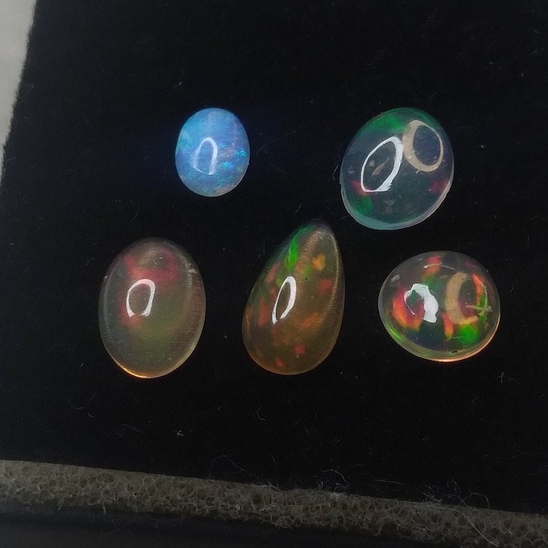 May include: Five iridescent opal gemstones of various shapes and sizes. The opals are a mix of green, blue, red, and white.