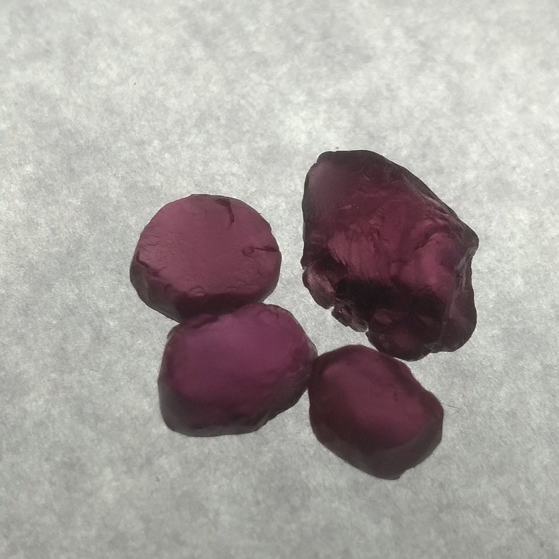 May include: Four deep red gemstones, three are round and one is irregularly shaped.