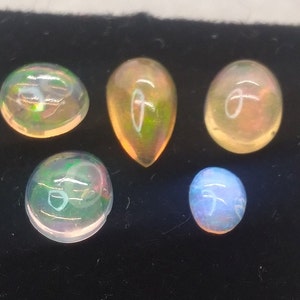 May include: Five opal gemstones of various shapes and sizes. The opals are iridescent with shades of green, blue, and orange.
