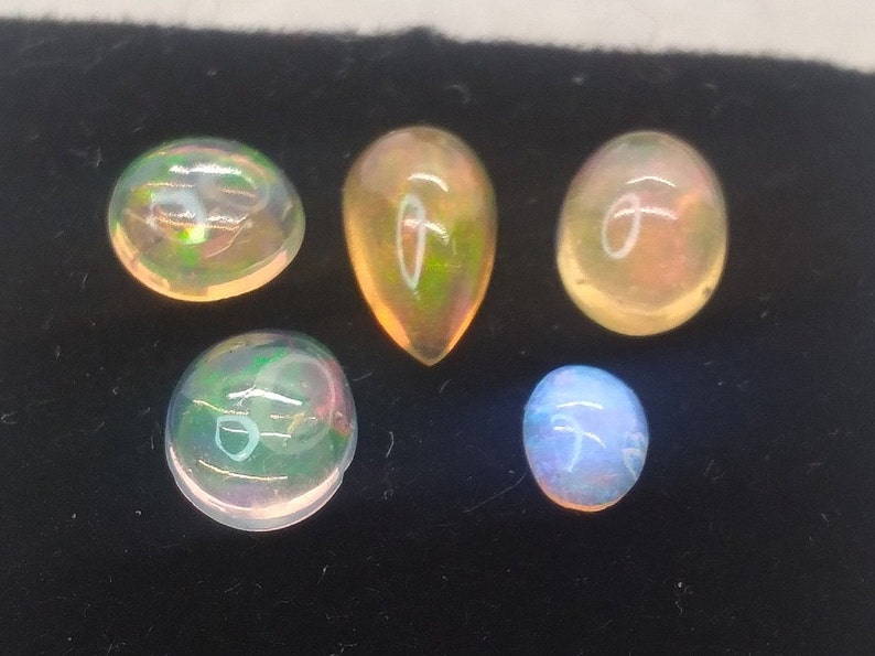 May include: Five opal gemstones of various shapes and sizes. The opals are iridescent with shades of green, blue, and orange.