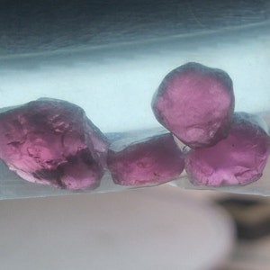 May include: Four pink gemstones, possibly amethyst, in a clear plastic bag. The gemstones are faceted and have a translucent appearance.