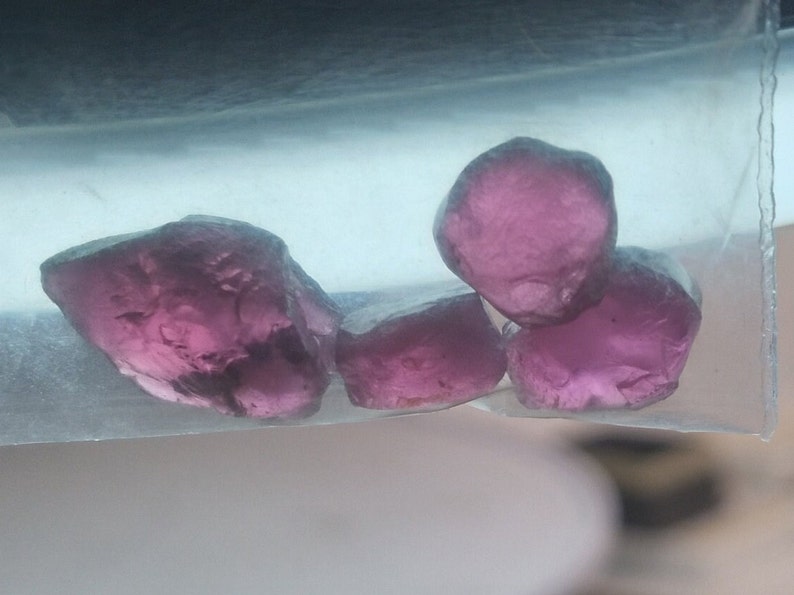 May include: Four pink gemstones, possibly amethyst, in a clear plastic bag. The gemstones are faceted and have a translucent appearance.