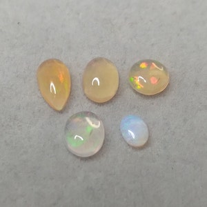 May include: Five opal gemstones in various shapes and sizes. The gemstones are a mix of white, light yellow, and iridescent colors.
