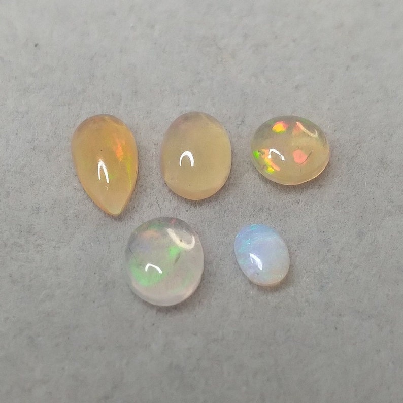 May include: Five opal gemstones in various shapes and sizes. The gemstones are a mix of white, light yellow, and iridescent colors.