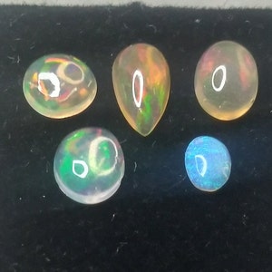 May include: Five opal gemstones of various shapes and sizes. The opals are iridescent with flashes of green, blue, and orange.