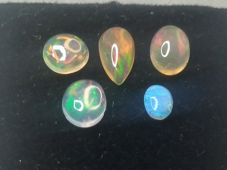 May include: Five opal gemstones of various shapes and sizes. The opals are iridescent with flashes of green, blue, and orange.