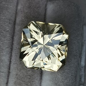 May include: A light yellow gemstone with a square cut and a star-like pattern in the centre.