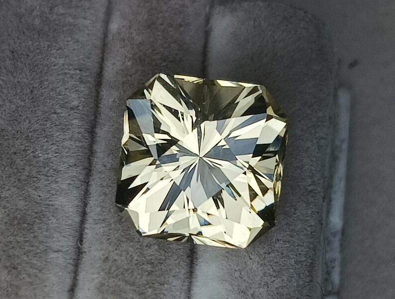 May include: A light yellow gemstone with a square cut and a star-like pattern in the centre.