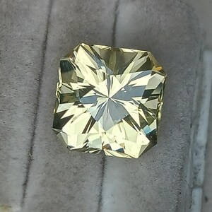 May include: A light yellow gemstone with a square shape and many facets.