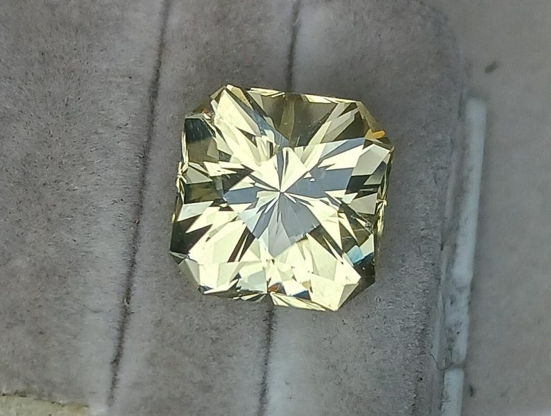 May include: A light yellow gemstone with a square shape and many facets.