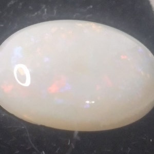 Puede incluir: Una piedra preciosa de ópalo ovalada blanca con destellos iridiscentes de color.