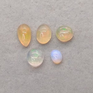 May include: Five opal gemstones in various shapes and sizes. The gemstones are a mix of white, yellow, and green.