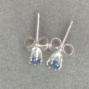 Puede incluir: Un par de pendientes de plata con una peque&ntilde;a piedra preciosa azul en cada uno. Los pendientes tienen un dise&ntilde;o simple y cl&aacute;sico.