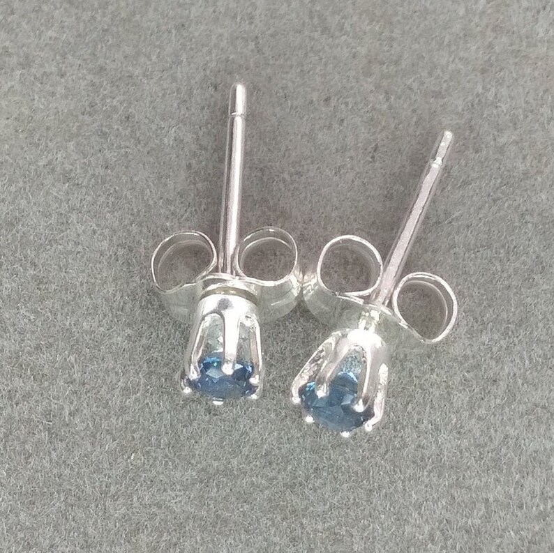 Puede incluir: Un par de pendientes de plata con una peque&ntilde;a piedra preciosa azul en cada uno. Los pendientes tienen un dise&ntilde;o simple y cl&aacute;sico.