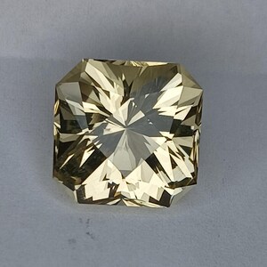 May include: A light yellow gemstone with a square shape and a faceted cut. The gemstone has a star-like pattern in the centre.
