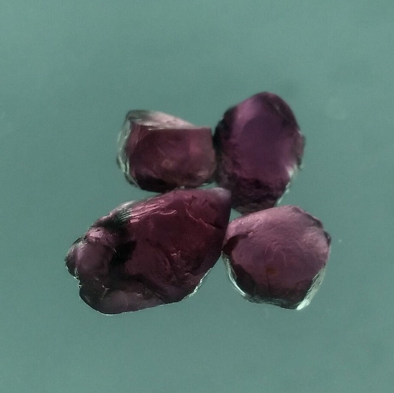 May include: Four small, faceted, purple gemstones. The gemstones are irregularly shaped and have a glossy finish.