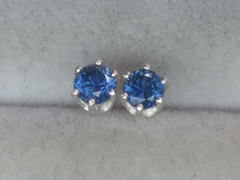 Puede incluir: Un par de pendientes de plata con una piedra preciosa redonda azul en cada uno.
