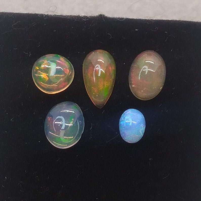 May include: Five opal gemstones of various shapes and sizes. The opals are iridescent with shades of blue, green, and orange.