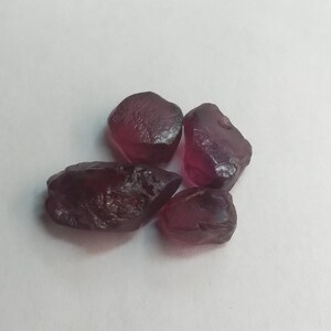 May include: Four rough, dark red gemstones, likely garnets, with irregular shapes and a glossy finish.