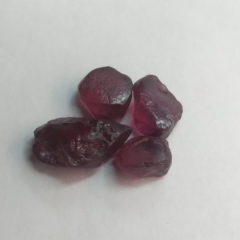 May include: Four rough, dark red gemstones, likely garnets, with irregular shapes and a glossy finish.